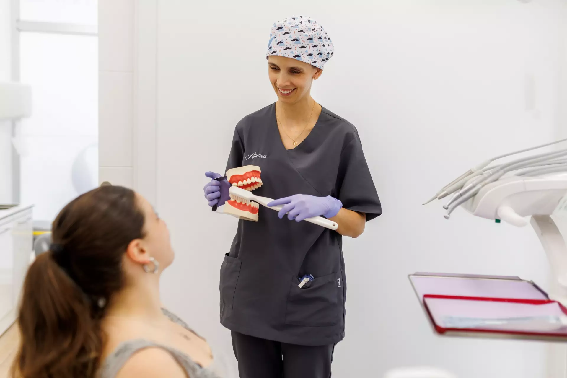 Mujer con una reproducción de una dentadura y un cepillo de dientes explicando a una paciente cómo lavarse los dientes