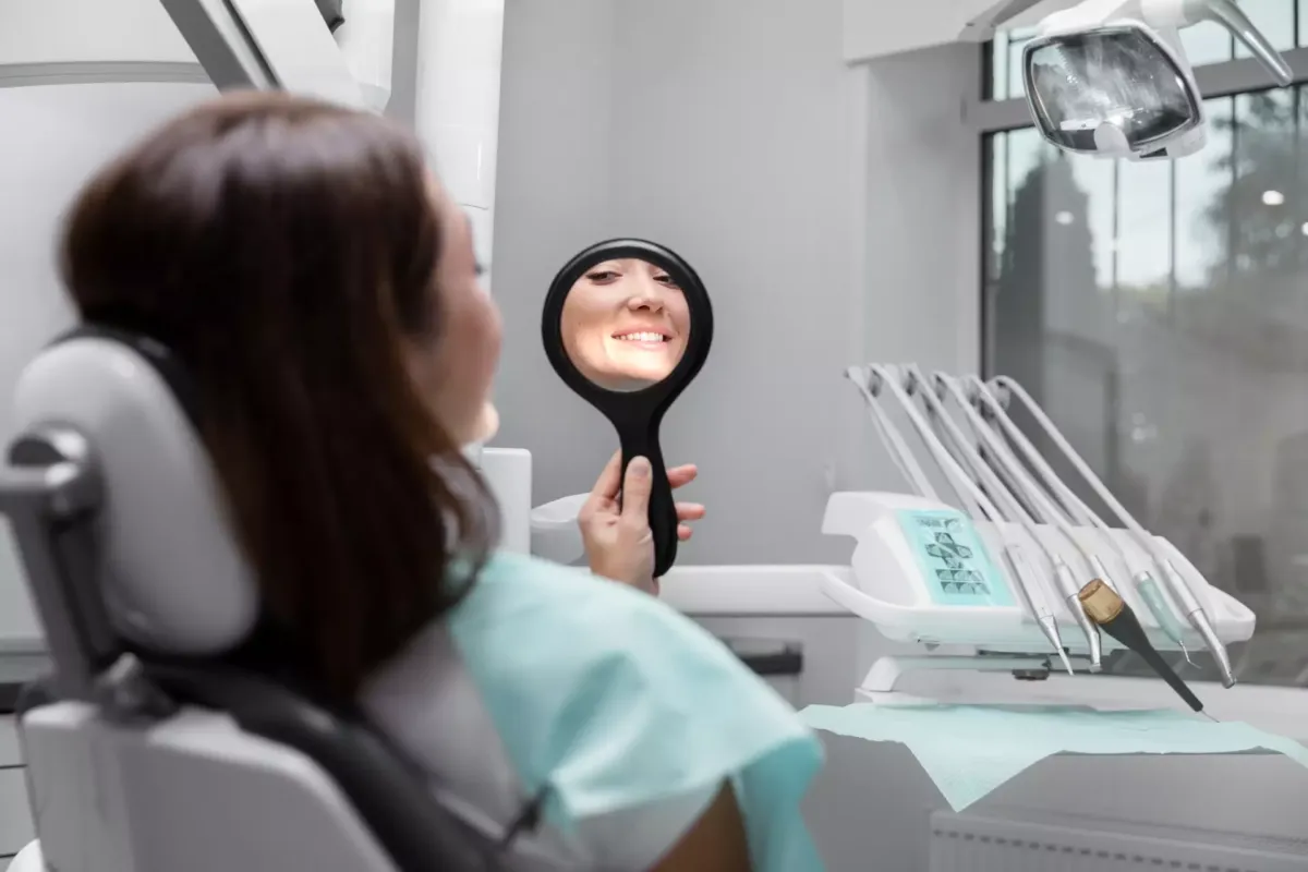 Mujer sentada en un sillón de clínica dental mirándose en un espejo de mano